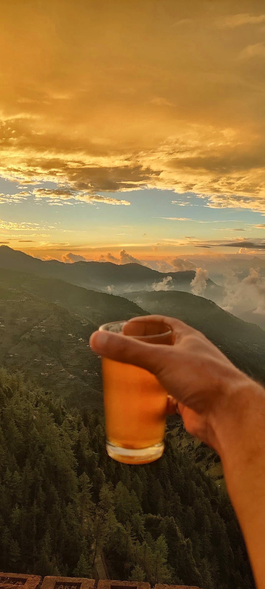 A glass of tea held up against the sunset over the hills at Pinewood